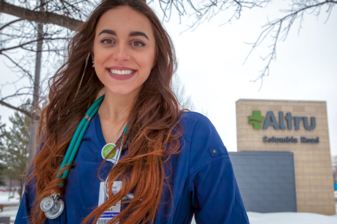 Nursing student stands in front of healthcare facility sign