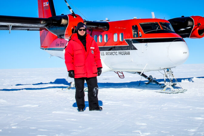 Student standing in arctic in front of plane