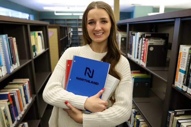 Student stands in library with Northland notebook