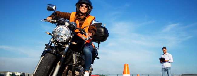 Student riding a motorcycle while an instructor evaluates the ride